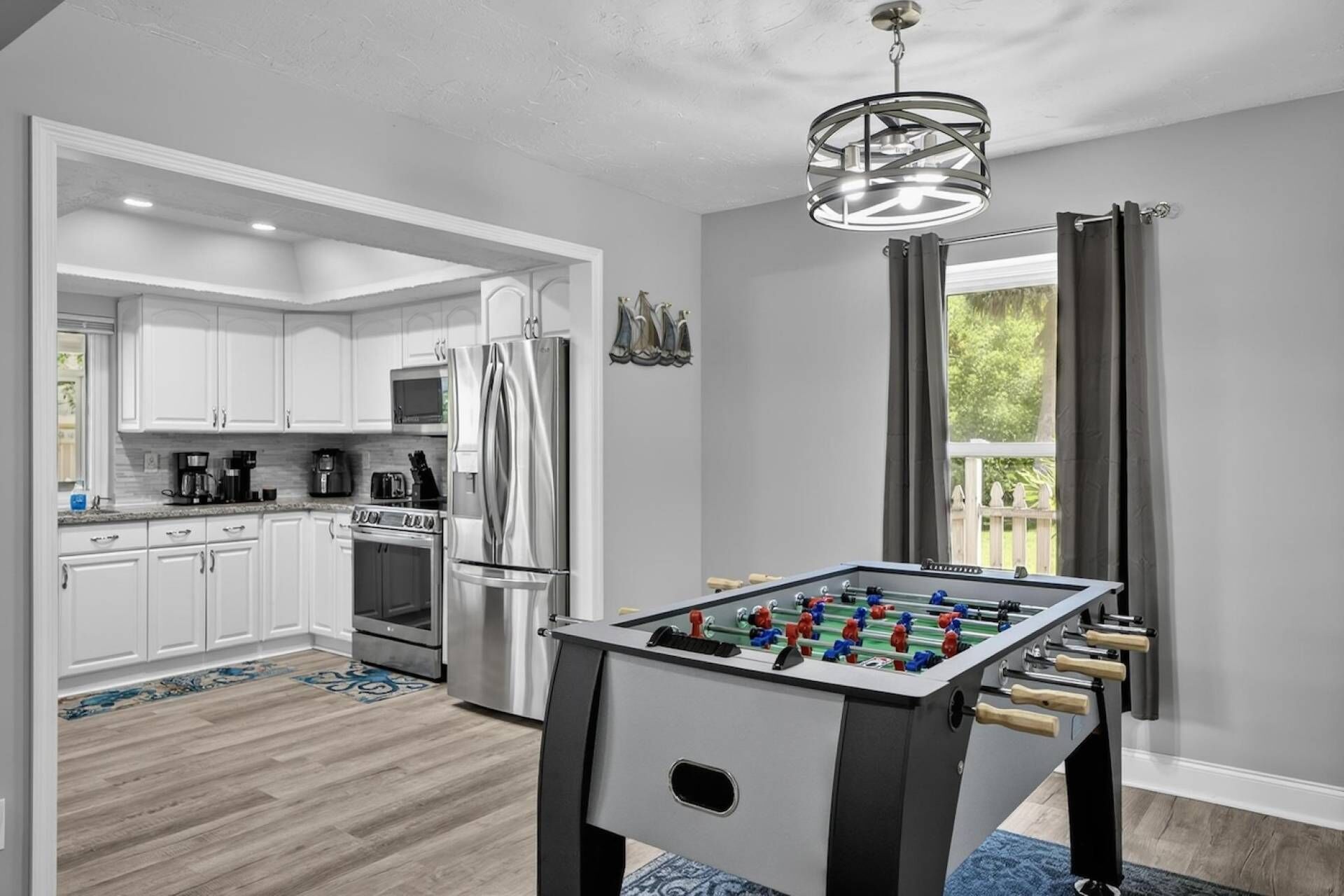 A modern kitchen with white cabinets, stainless steel appliances, and a foosball table.