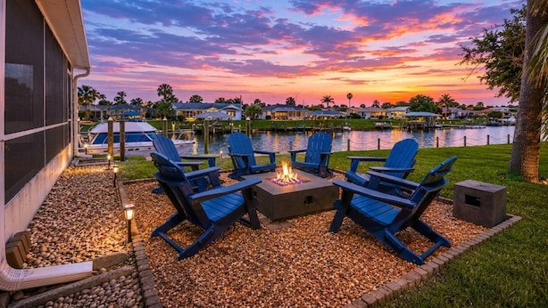 A waterfront patio with Adirondack chairs, a fire pit, and a view of a lake at sunset. - Anchors Landing Waterfront Home | Dock | Foosball | Fire Pit | Close To The Beach | Dog Friendly (Palm Coast)