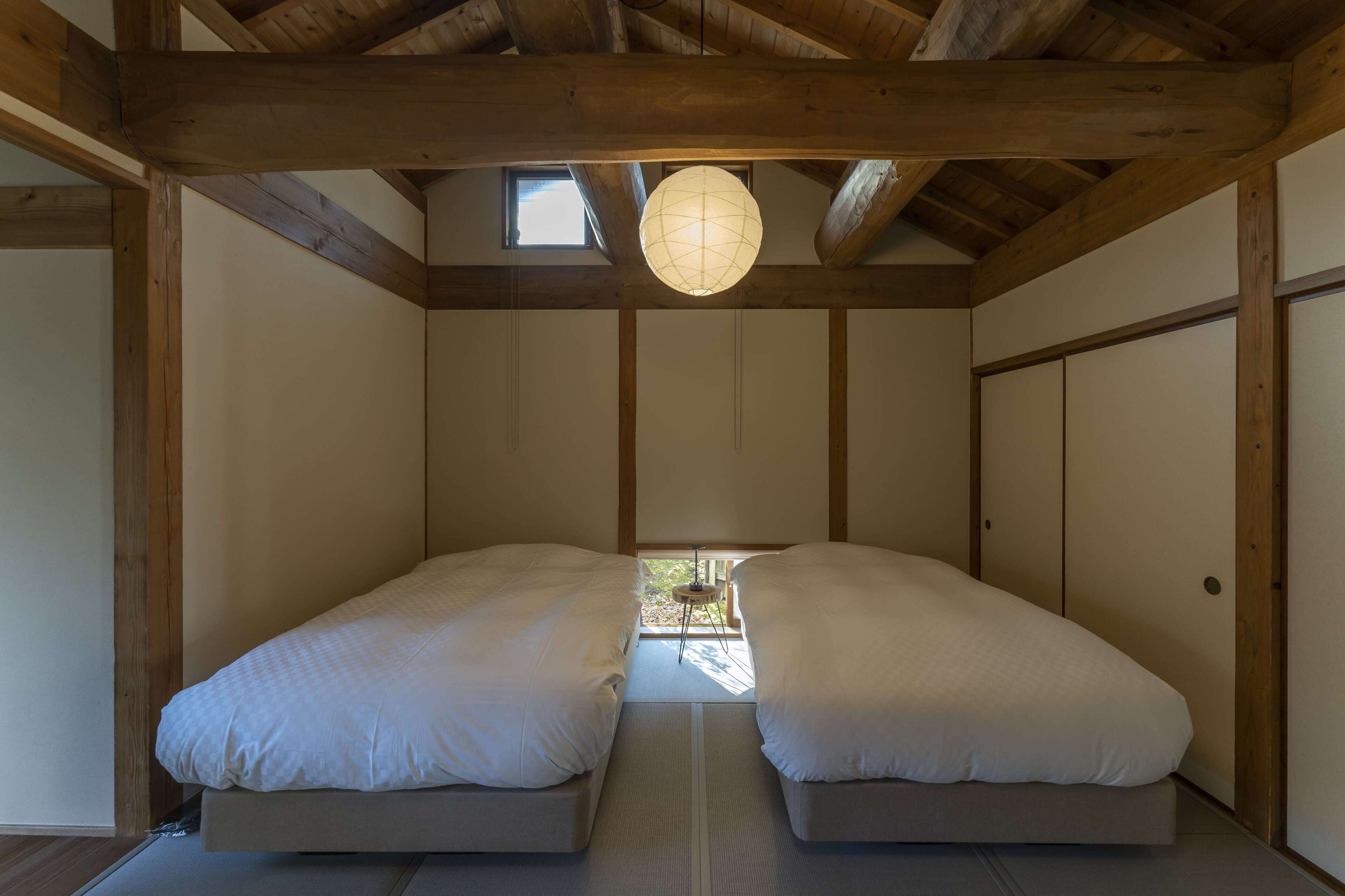 A room with two beds, wooden beams, a hanging light fixture, and a small table.