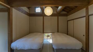 A room with two beds, wooden beams, a hanging light fixture, and a small table.