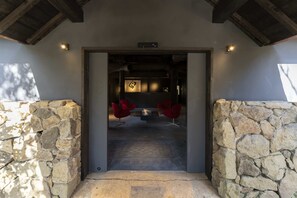 Una entrada de paredes de piedra que conduce a una habitación con chimenea, dos sillas rojas y suelo de piedra.
