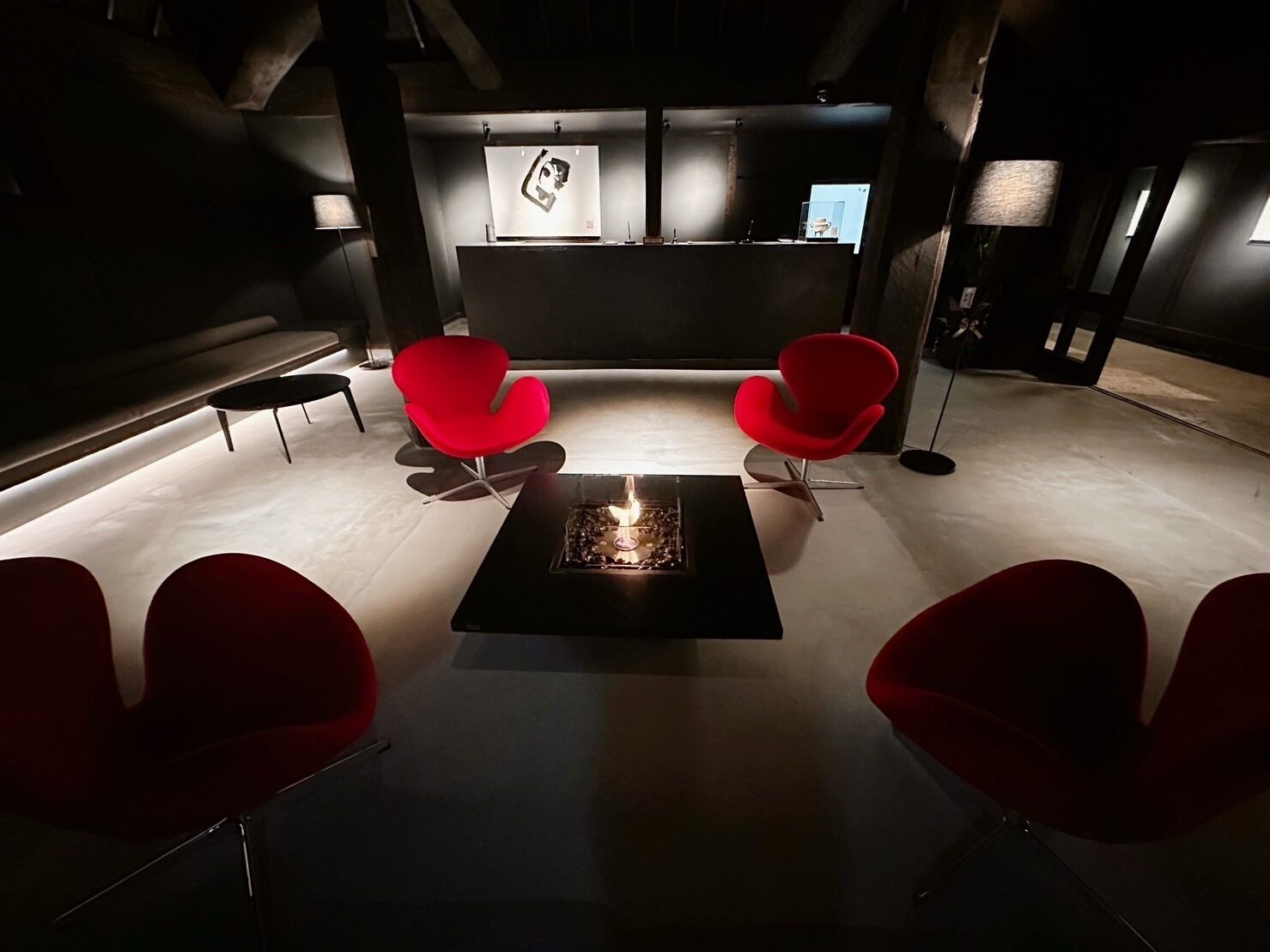 A modern lounge area with a central fire feature, red chairs, and artwork on the walls.