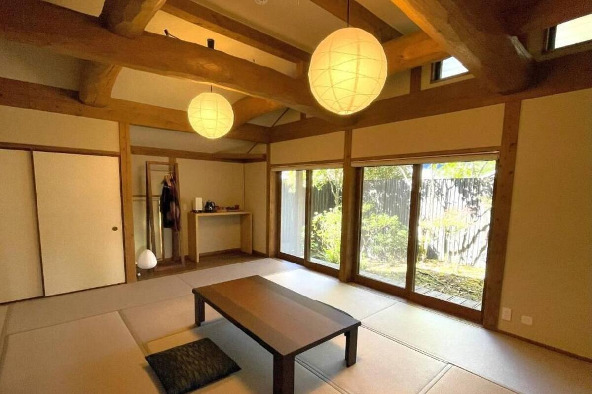 A traditional Japanese room with tatami flooring, a low wooden table, sliding doors, and large windows with a view of greenery.