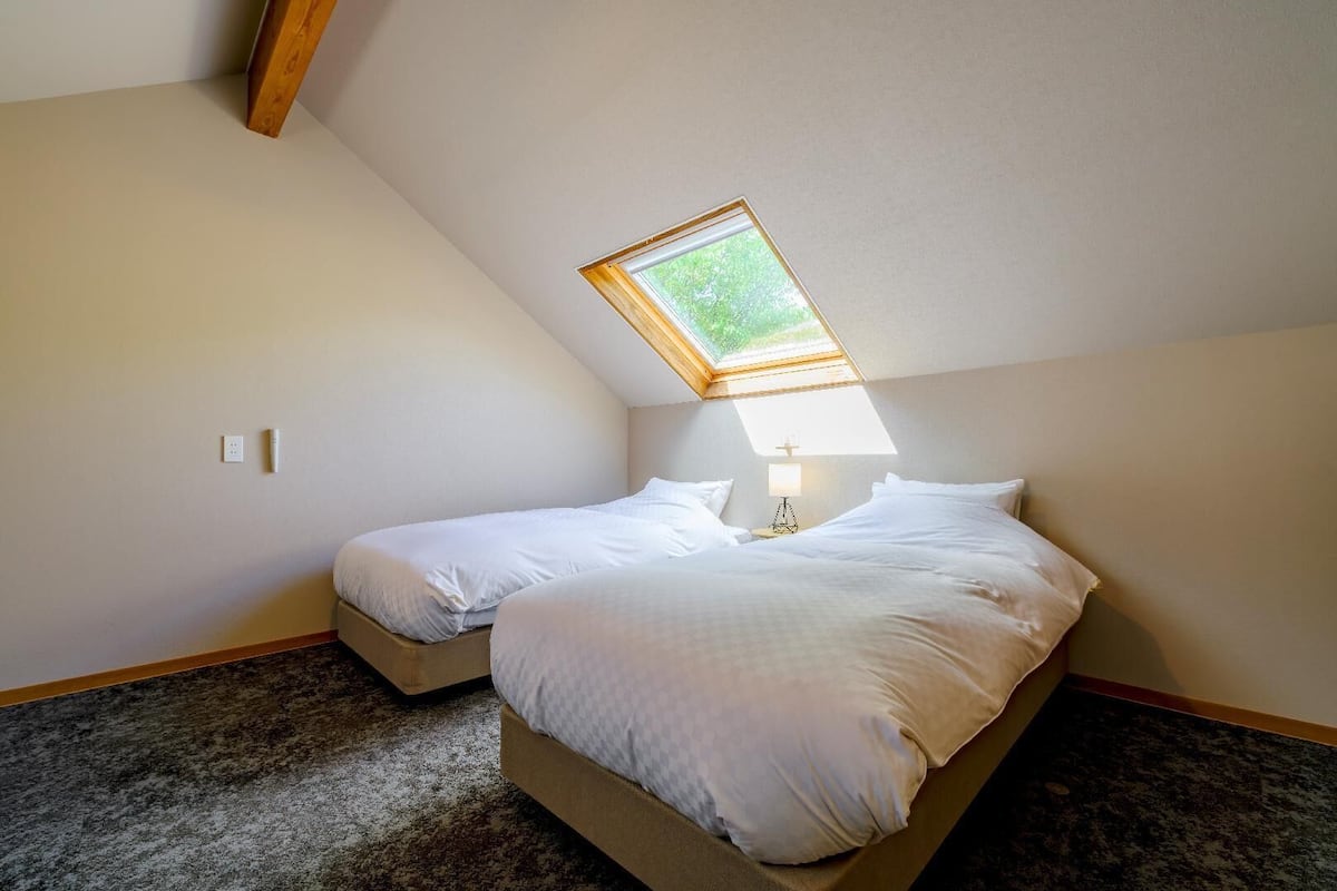 Une petite pièce avec deux lits, un toit en pente et une lucarne, ainsi qu’une lampe.