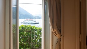 A room with a view of a boat on a lake, a balcony with greenery, and a door. - Casa Margherita in Varenna (Varenna)
