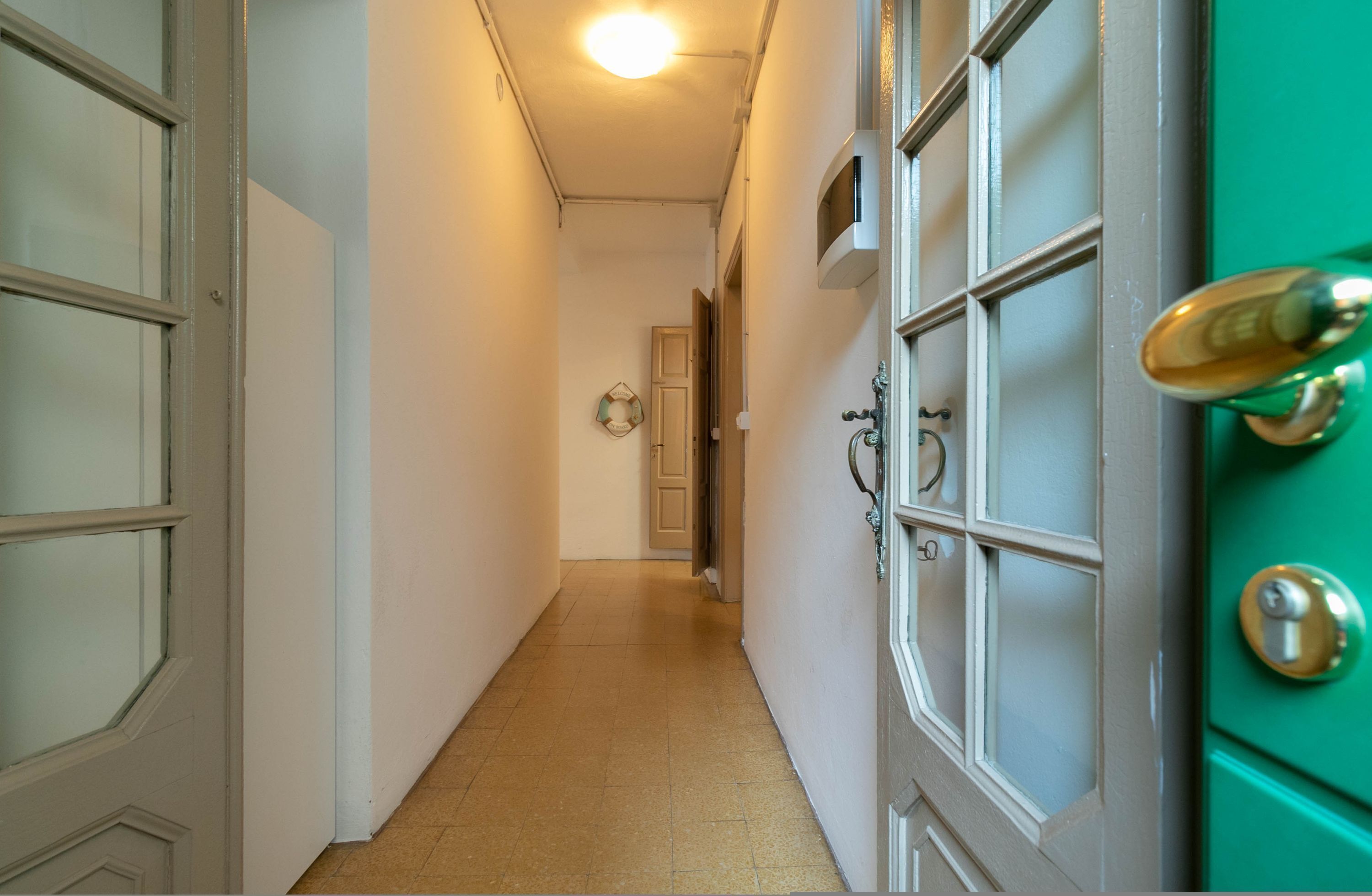 Um corredor com uma porta verde, uma porta branca e um aparelho de iluminação no teto.