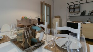 A dining area with a wooden table set for two, white chairs, and a kitchen in the background. - Casa Margherita in Varenna (Varenna)