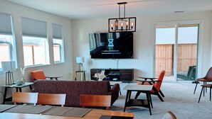 A modern living room with a large flat-screen TV, a dining area with a wooden table and chairs, and a cozy seating area with a sofa and armchairs. - Modern, Spacious, Family friendly & Relaxing Home in Sparks, NV. (Sparks)
