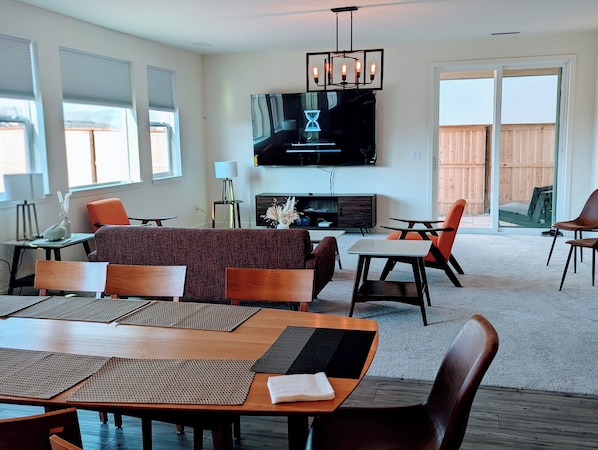 Una sala de estar moderna con un televisor de pantalla plana grande, un comedor con mesa y sillas de madera, y una zona de estar acogedora con sofá y sillones.