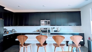 A modern kitchen with dark cabinets, a central island with chairs, and a microwave. - Modern, Spacious, Family friendly & Relaxing Home in Sparks, NV. (Sparks)
