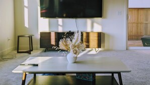 A modern living room with a flat-screen TV mounted on the wall, a white coffee table with a vase of dried flowers, and a small side table. - Modern, Spacious, Family friendly & Relaxing Home in Sparks, NV. (Sparks)