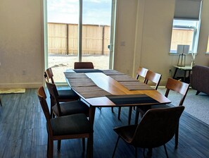 Ein geräumiges Zimmer mit einem langen Esstisch, großen Fenstern und Blick auf einen hölzernen Zaun.