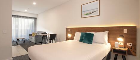 Une chambre d’hôtel avec un grand lit, un bureau, des chaises, une vue sur la plage et un tableau encadré au mur.