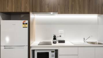 A modern kitchen with a white refrigerator, a Panasonic microwave, a coffee machine, and a sink.