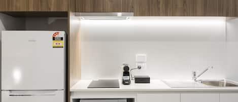 A modern kitchen with a white refrigerator, a Panasonic microwave, a coffee machine, and a sink.