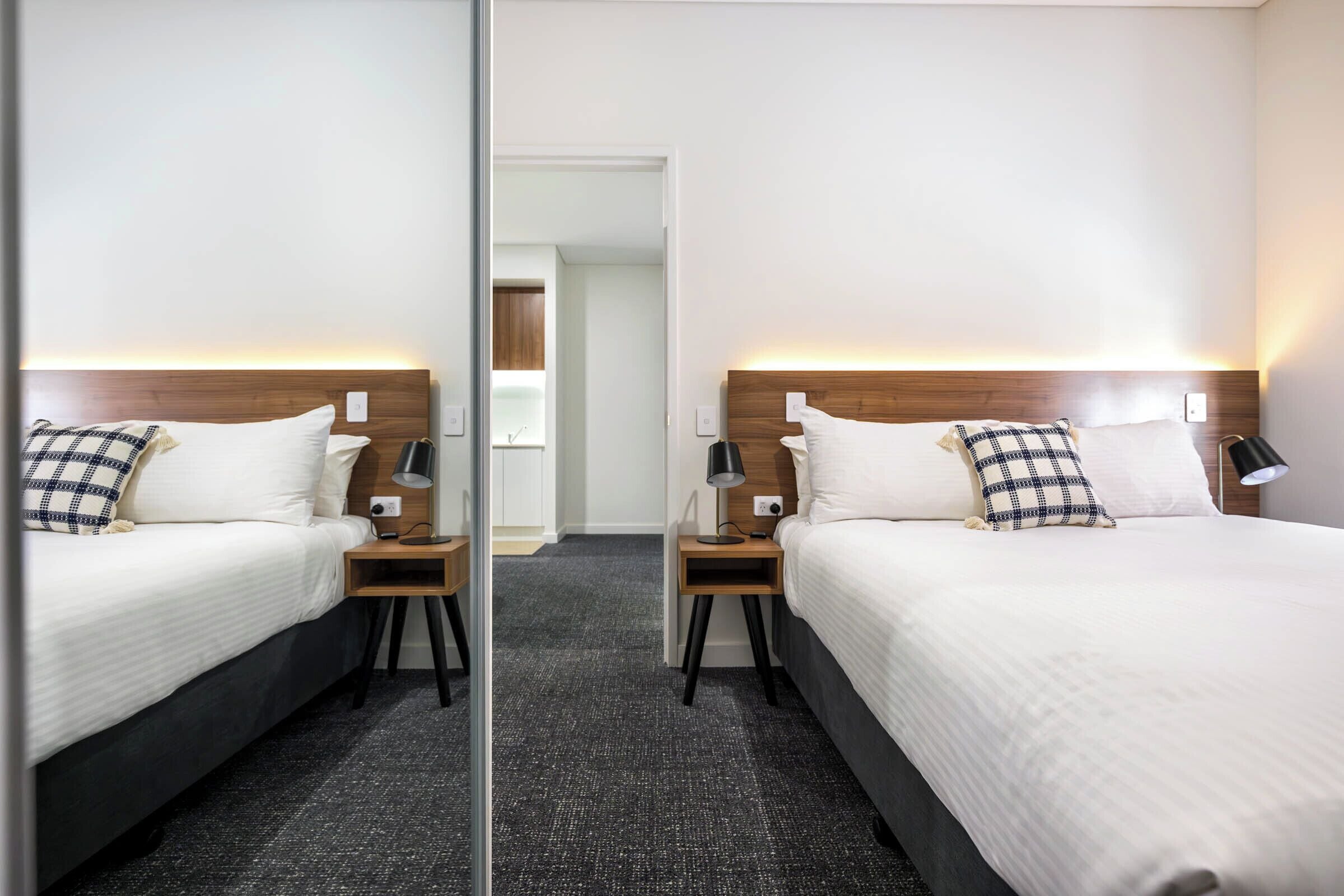 Een hotelkamer met spiegels, twee bedden, elk met een houten hoofdbord, witte beddengoed en een geruit kussen.