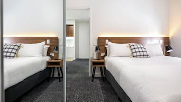 A mirrored hotel room with two beds, each with a wooden headboard, white bedding, and a checkered pillow.
