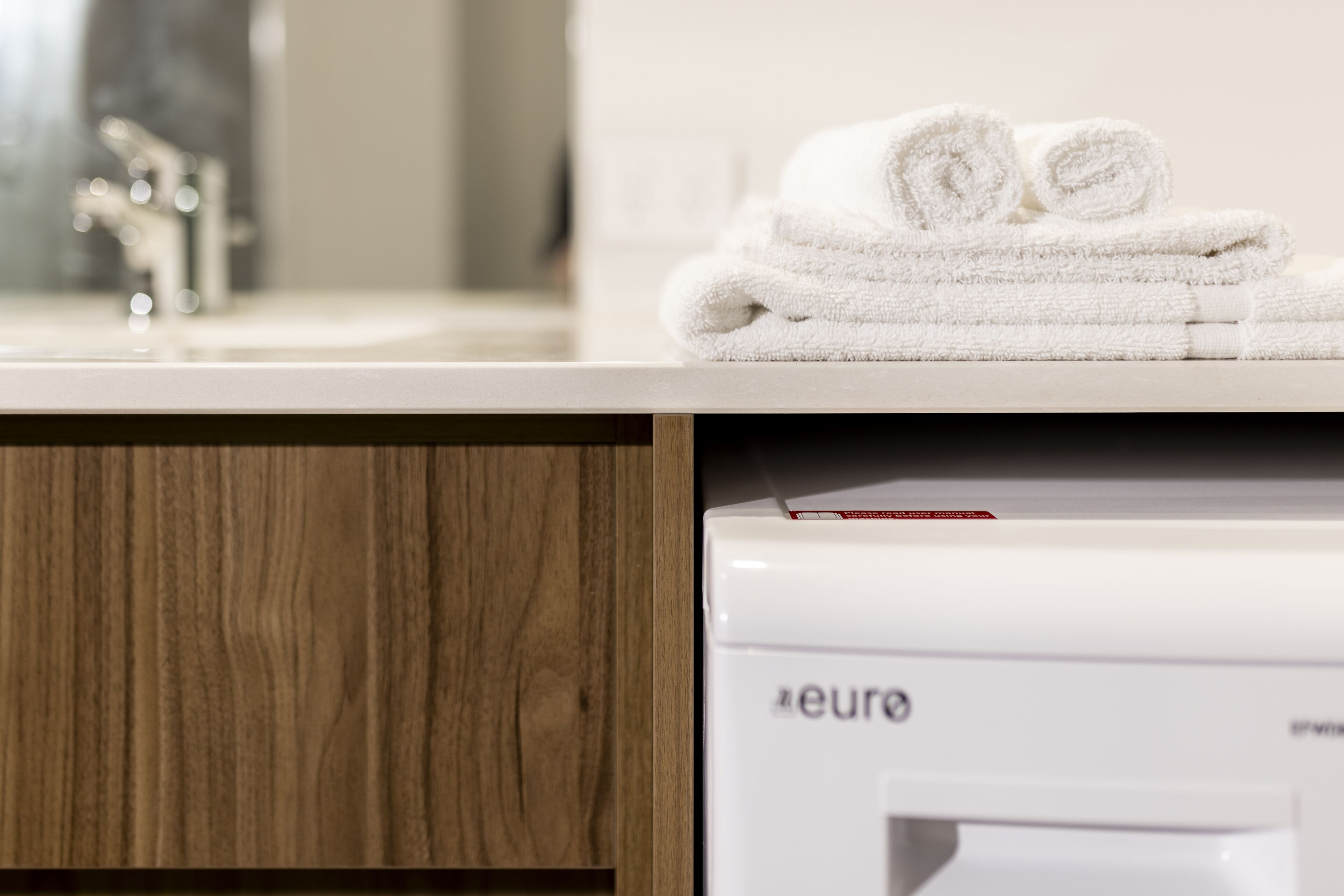 A bathroom with a wooden vanity, a white sink, and a white towel stack.