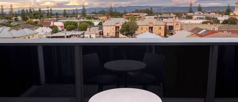 A rooftop terrace with two chairs and a table, overlooking a cityscape with buildings and trees.