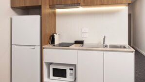 Cocina pequeña equipada con refrigerador, microondas, lavamanos y armarios de madera.