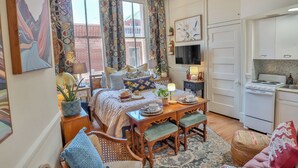 A cozy bedroom with a bed, bedside table, lamp, and a view of a brick building. - Against the Riverwalk/King (San Antonio)