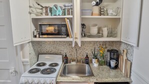 A compact kitchen with a stove, microwave, sink, and various kitchen utensils and appliances. - Against the Riverwalk/King (San Antonio)