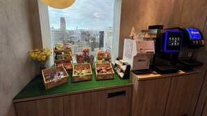 A snack display with various packaged goods, a coffee machine, and a vending machine in a room with a city view through a large window. - Sky Gate Hotel (Taipei)