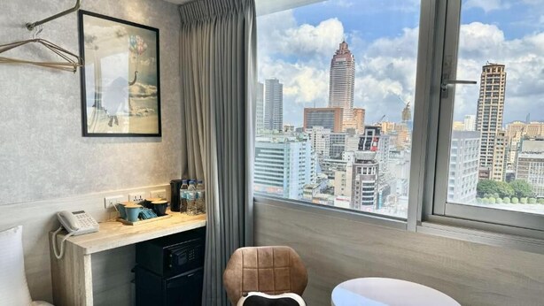 A hotel room with a city view, a desk with a phone, a chair, and a small table. - Sky Gate Hotel (Taipei)
