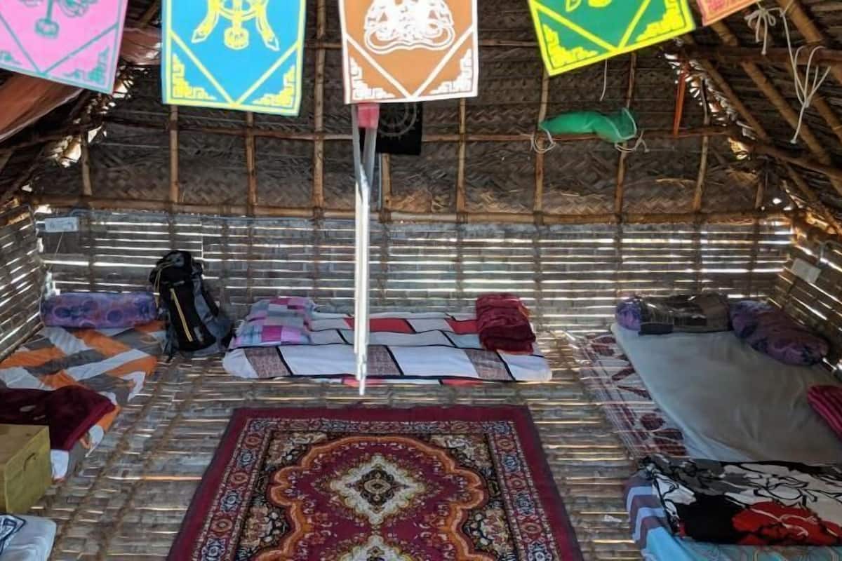 A room with a thatched roof, a central pole, a patterned rug, and various items scattered around.