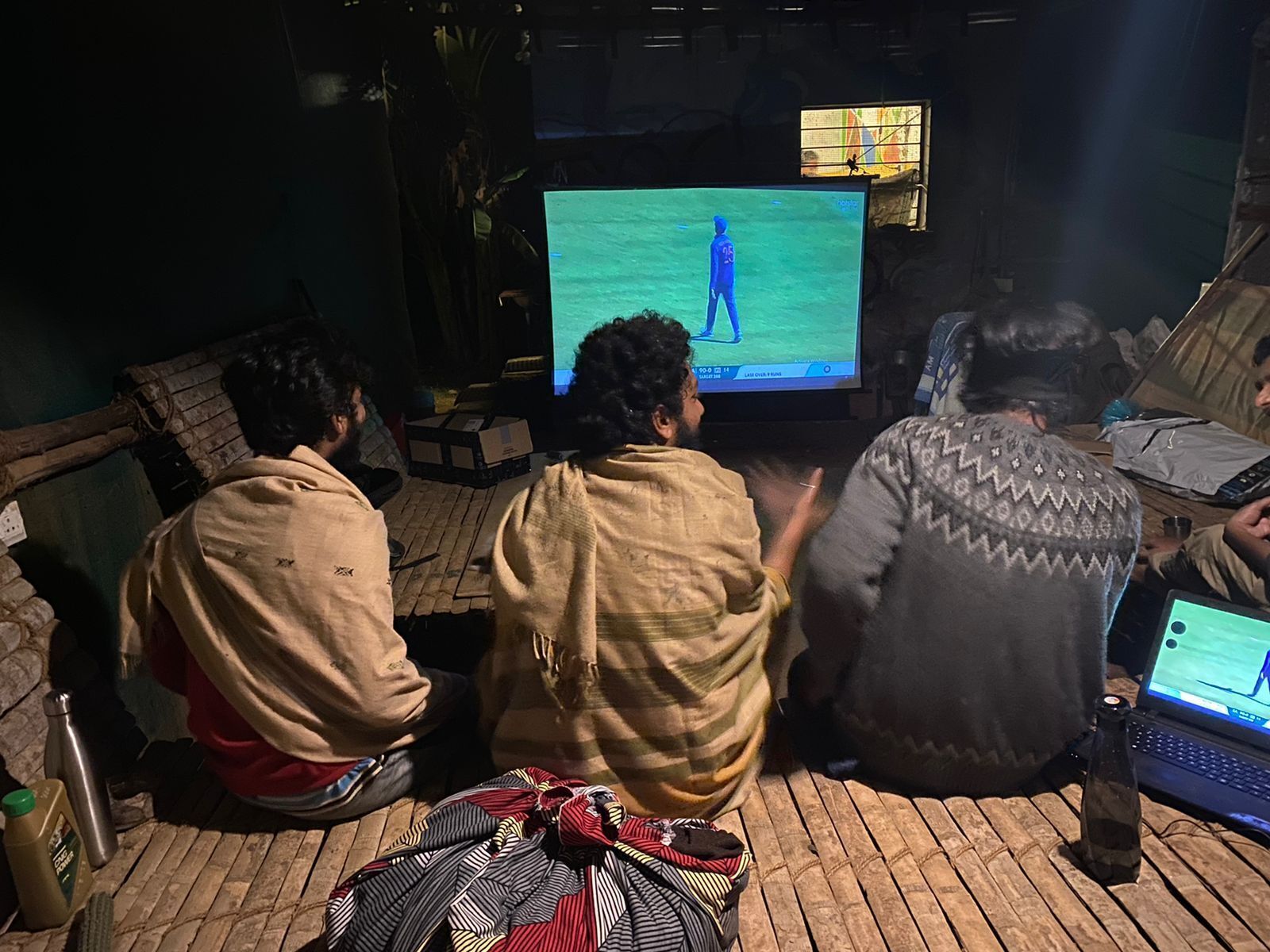 A group of people sitting on a wooden floor, watching a screen displaying a video game.