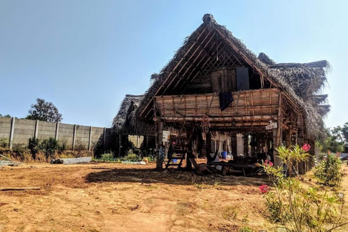 A rustic thatched-roof house with a wooden structure, a dirt ground, and some vegetation around.