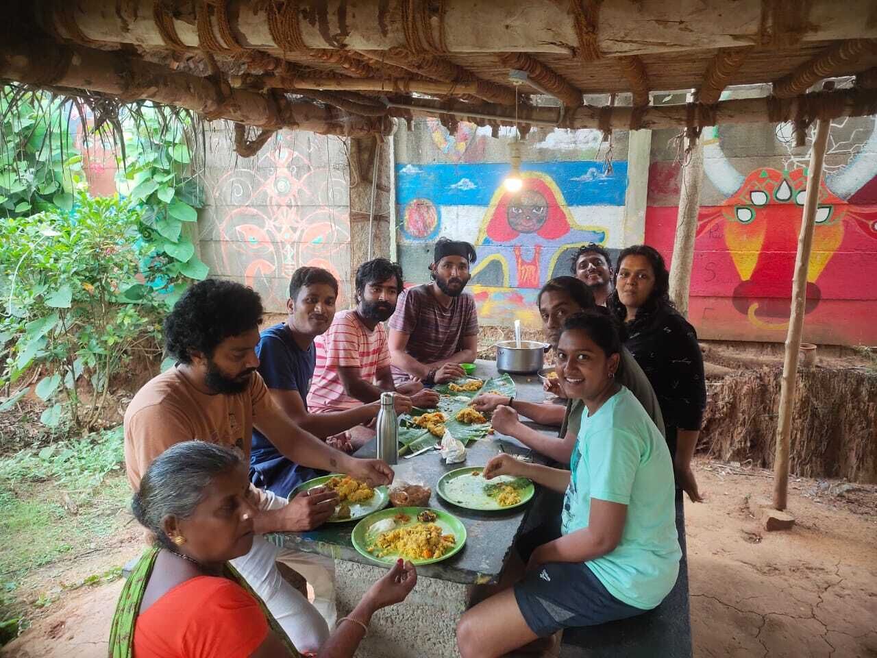 Un groupe de personnes est assis autour d’une table à l’extérieur et prend son repas.
