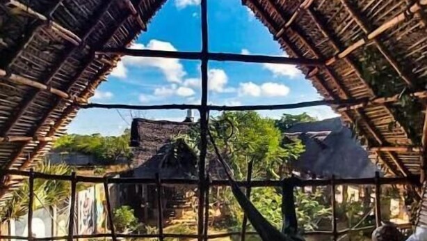 A thatched-roof structure with a central support beam, a green area in the foreground, and a view of the surrounding landscape. - Time Travellers Hostel (Tindivanam)