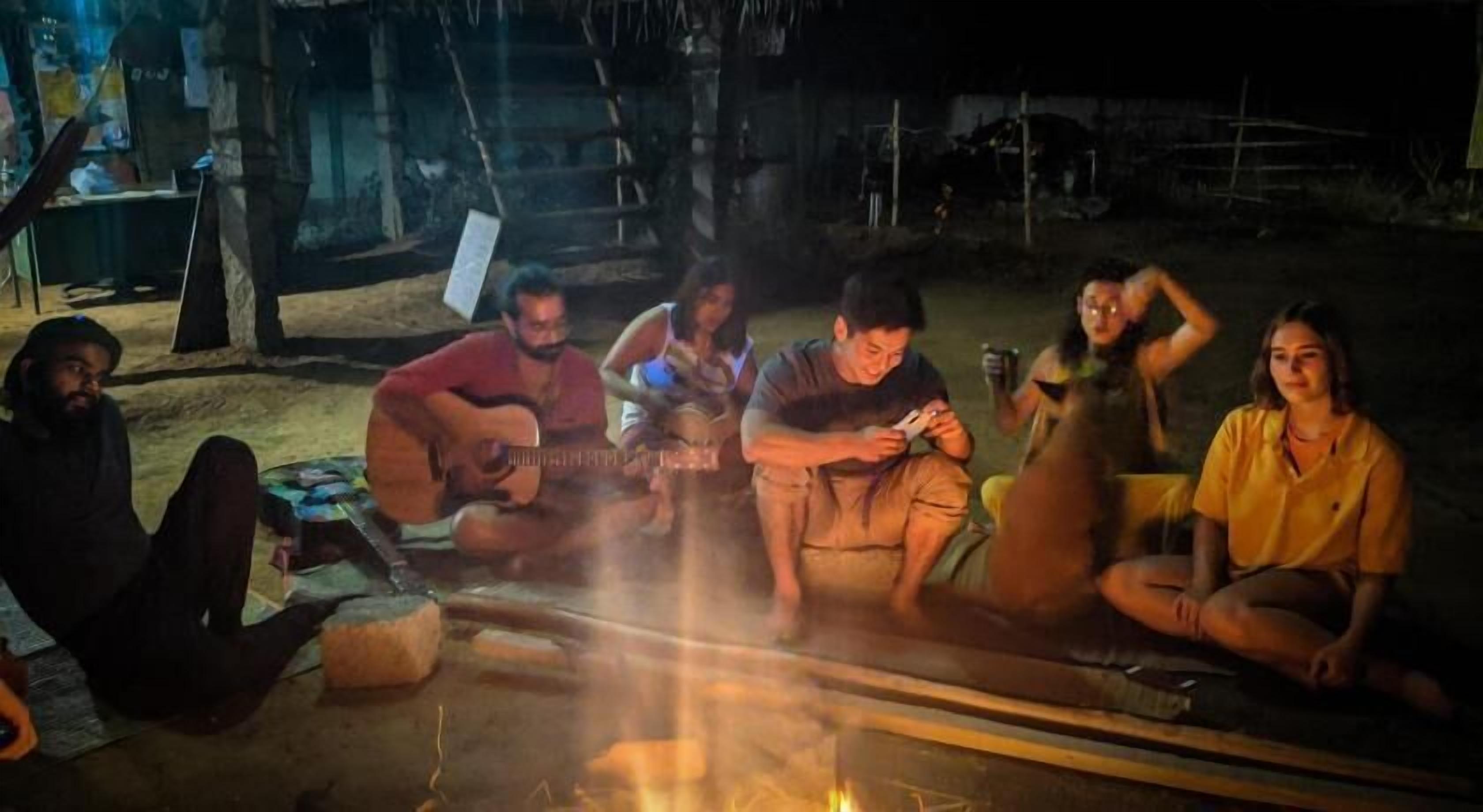 A group of people sitting around a campfire in an outdoor setting.