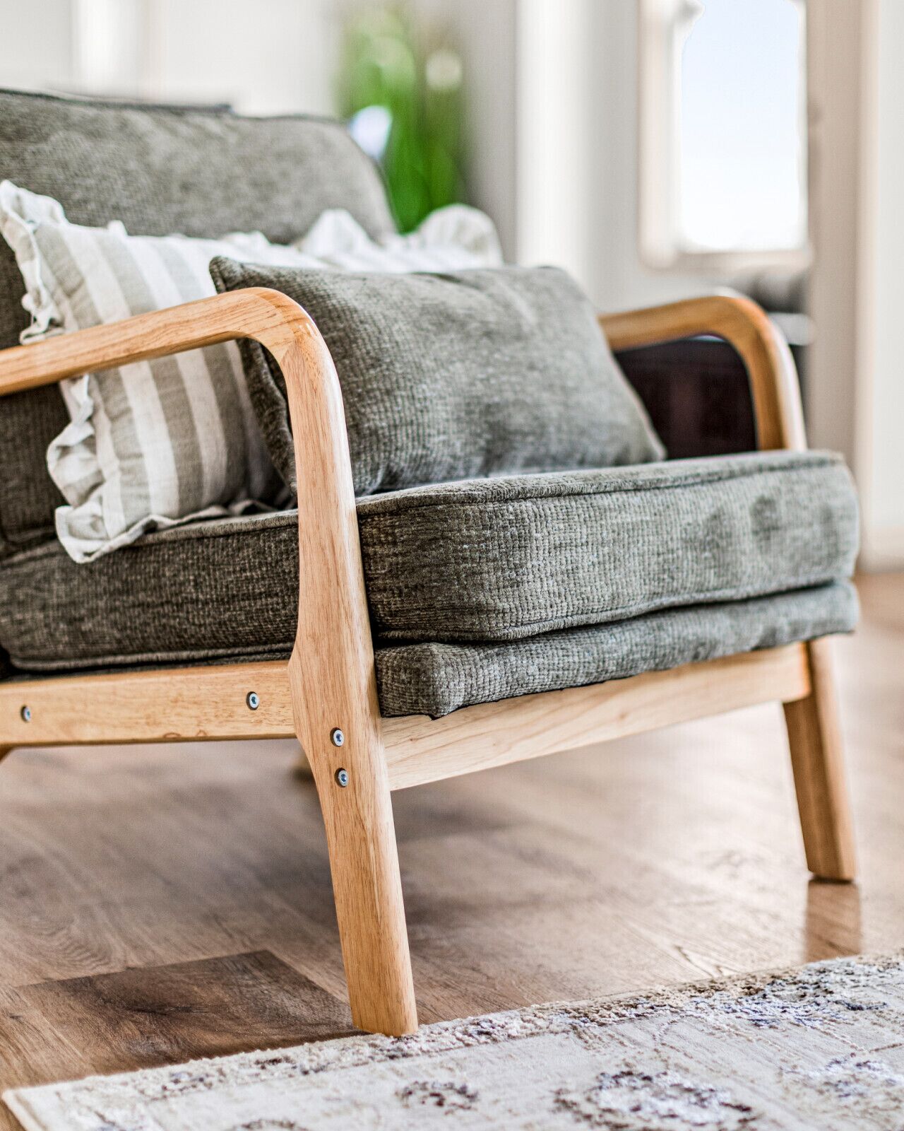 Een houten bank met grijze kussens en een gestreept kussen, op een houten vloer met een patroonrijk vloerkleed.