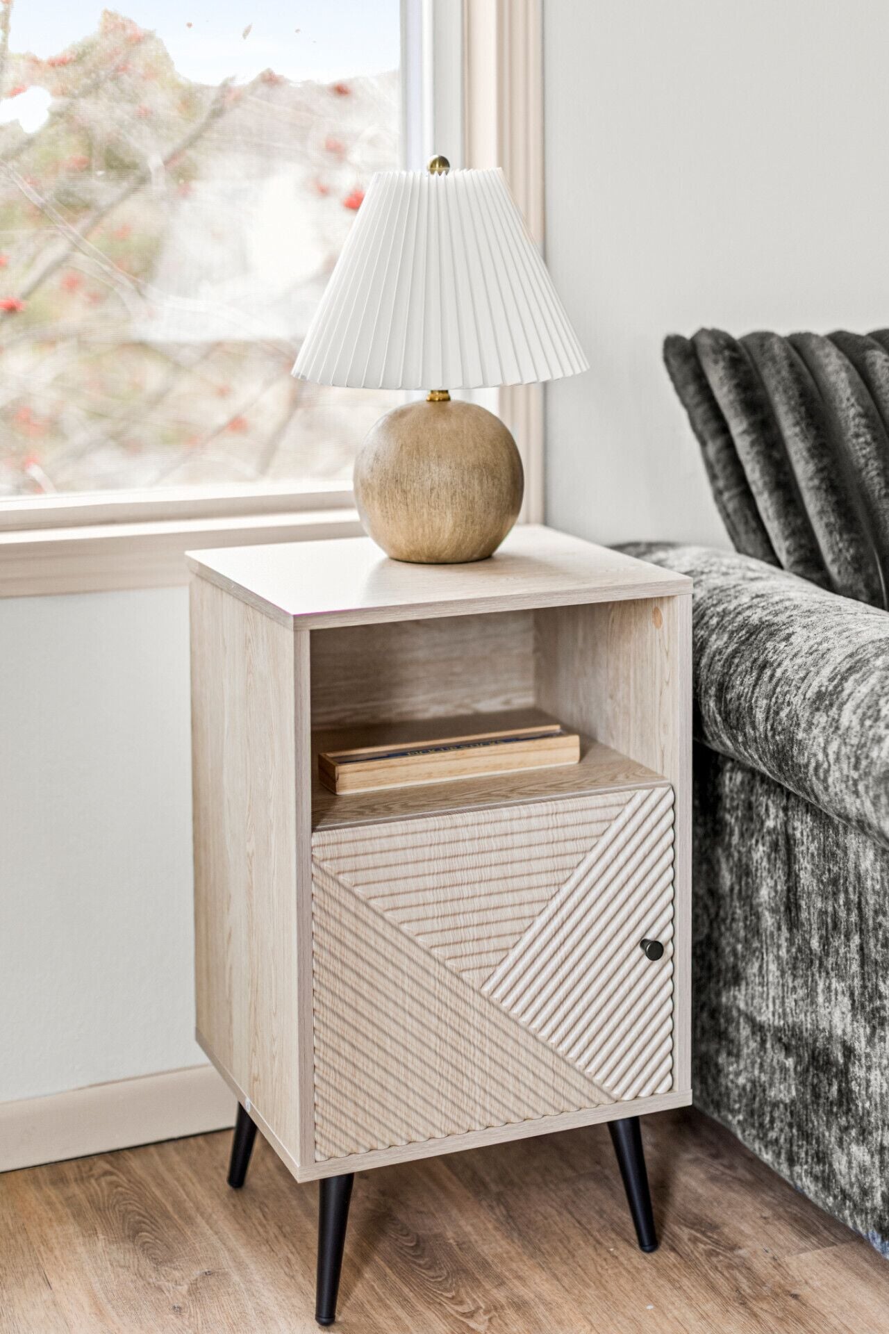 A wooden bedside table with a lamp, a drawer, and a geometric-patterned cabinet.