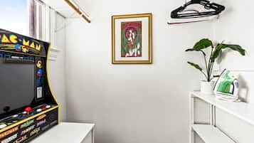Una habitación con una máquina de videojuegos Pac-Man, un cuadro en la pared y una planta en un estante.