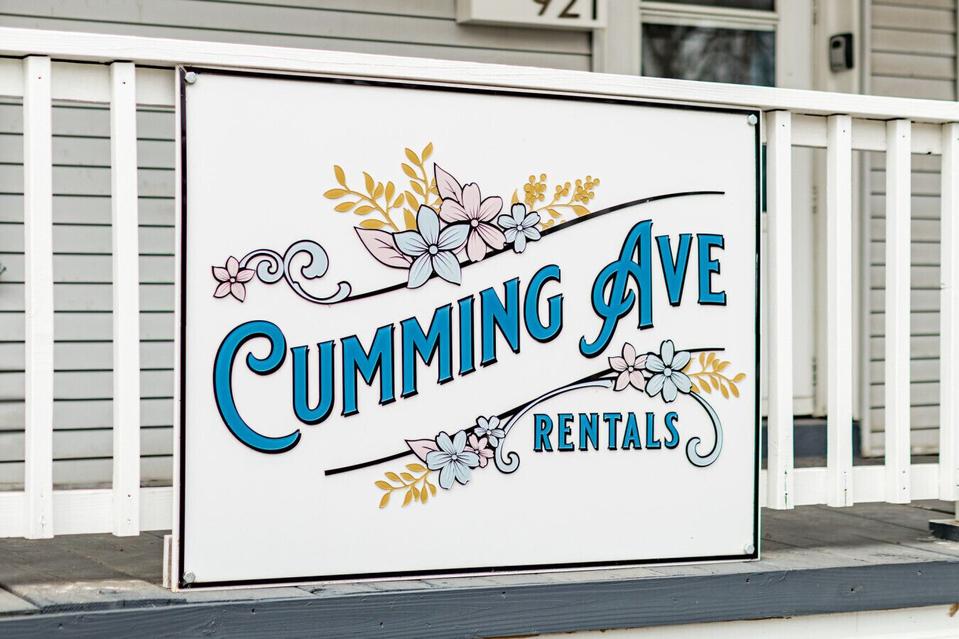 Letrero de Cumming Ave Rentals con detalles florales decorativos.