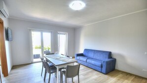Een moderne woonkamer met een eettafel, stoelen, een blauwe bank en een groot raam.