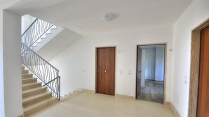 Een ruime hal met een houten deur, een trap met metalen leuningen en een zicht op een andere kamer.