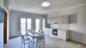 A modern kitchen with white cabinets, a dining table with chairs, and a large window. - Casa Ondina B: A welcoming apartment situated in a quiet location, a few minutes from the town center, with Free WI-FI. (Casal Velino)