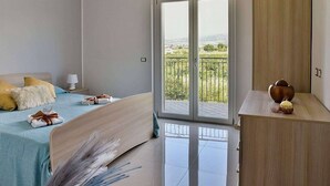 A bedroom with a bed, a nightstand, a dresser, and a balcony with a view. - Casa Ondina B: A welcoming apartment situated in a quiet location, a few minutes from the town center, with Free WI-FI. (Casal Velino)