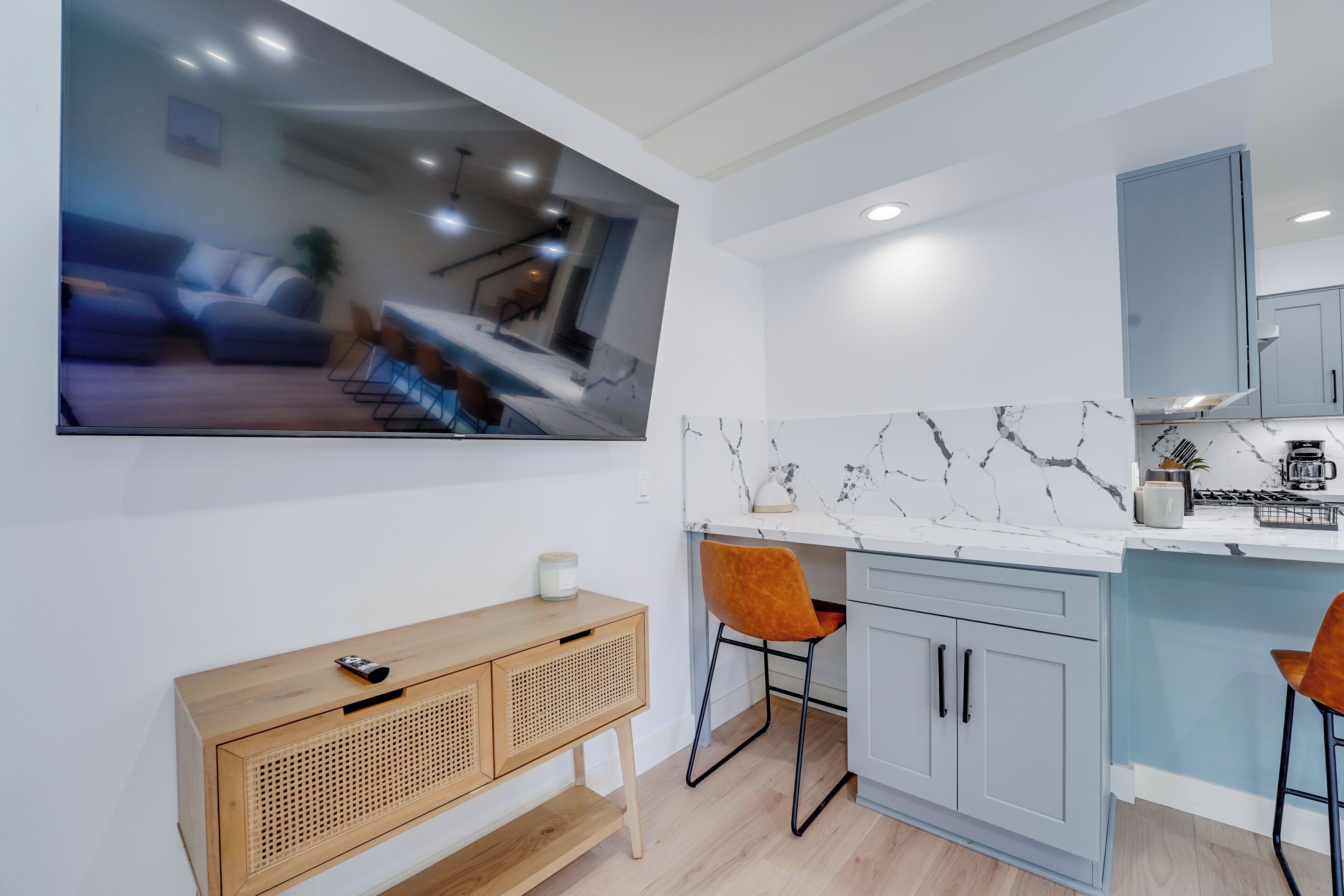 A modern kitchen with a marble backsplash, grey cabinets, and a wooden console table with a remote control.