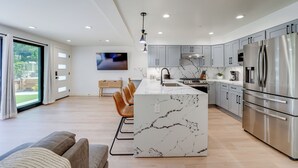 Een moderne keuken met een marmeren eiland, roestvrijstalen apparatuur en een groot raam met uitzicht op een tuin.