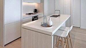 Uma cozinha moderna com armários brancos, uma ilha central com banquetas e um fogão embutido.