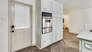 Una cocina moderna con armarios blancos, horno integrado y un refrigerador de acero inoxidable.