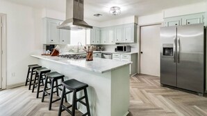Een moderne keuken met een centraal kookeiland, barkrukken, roestvrijstalen apparatuur en lichte kastjes.