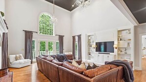 Een ruime woonkamer met een grote hoekbank, een flatscreen televisie en een witte mediakast.