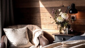 Ein gemütliches Zimmer mit Ledersessel, Holzwand, Nachttisch mit Lampe und Blumenvase.