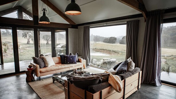 Ein geräumiges Wohnzimmer mit einem großen Fenster und Blick auf eine grüne Wiese. Es gibt ein Sofa und eine hölzerne Kommode.